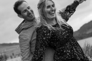 Black-and-white photo of a couple playfully moving their arms while laughing into nature