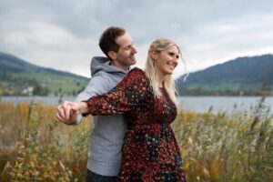 Young couple standing with outstretched arms in front of a lake while laughing into nature