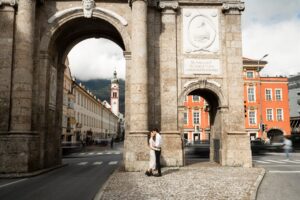 Young couple kissing in front of the stone arches of Innsbruck’s Triumphal Arch