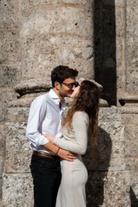 Young couple kissing in harsh light in front of a column while wearing sunglasses