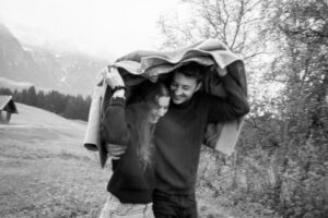 Black-and-white photo with motion blur of a couple sheltering beneath the man’s jacket in the rain