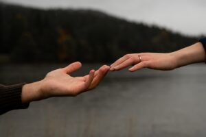 Close-up of an engaged couple’s hands touching in front of a lake and mountains with focus on the engagement ring