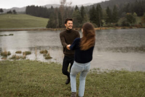 Couple spinning hand in hand in front of a lake while smiling at each other