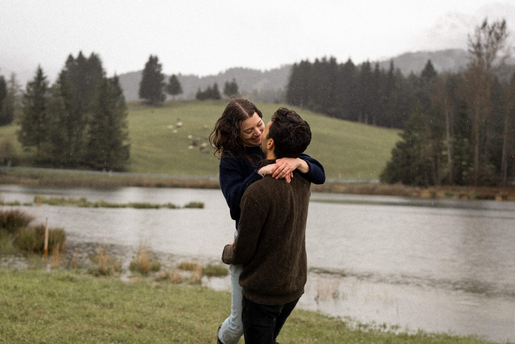 Medium close-up photo of a man lifting and twirling his fiancée while she smiles at him