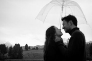 Low-angle black-and-white photo of a couple beneath an umbrella with focus on the background