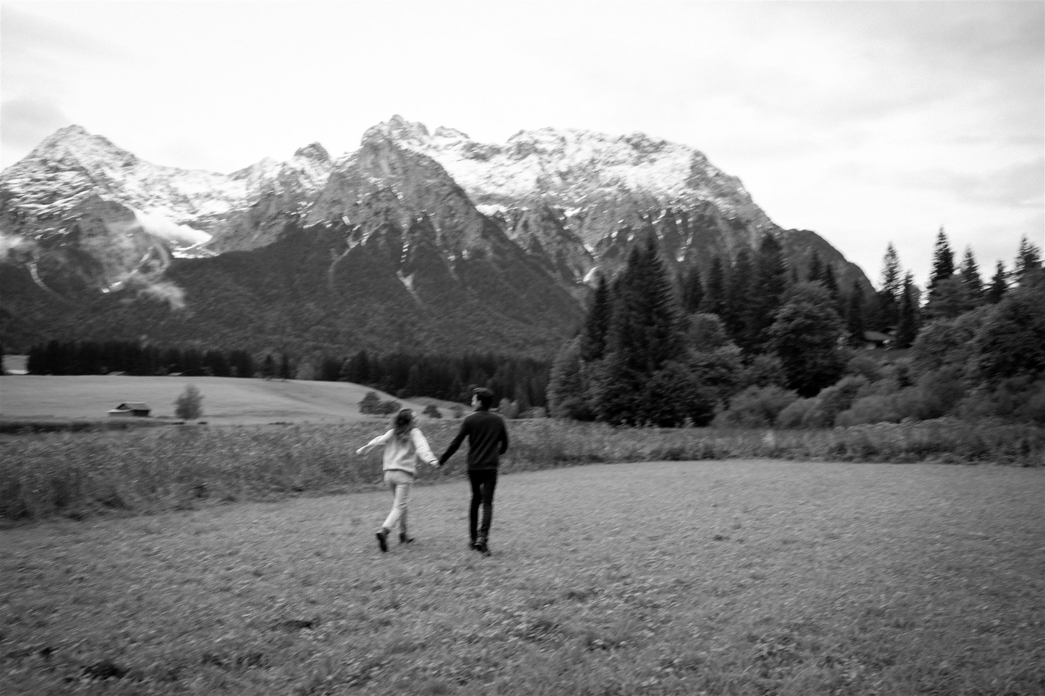 Young couple walking toward a lake with snowy mountains in the background and motion blur in black and white