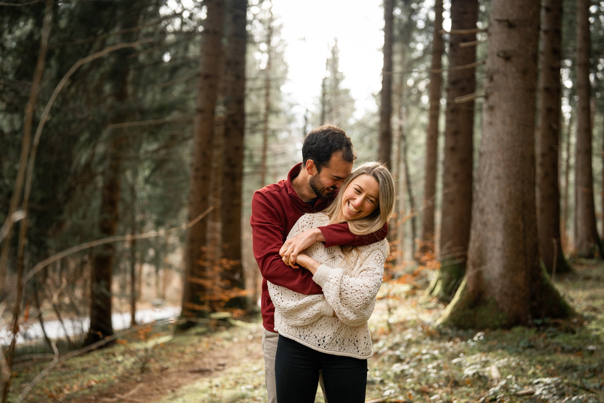 Man embracing his fiancé from behind while whispering into her ear and both laugh
