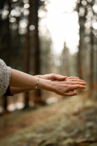 Side-view close-up of hands in the forest with a visible engagement ring
