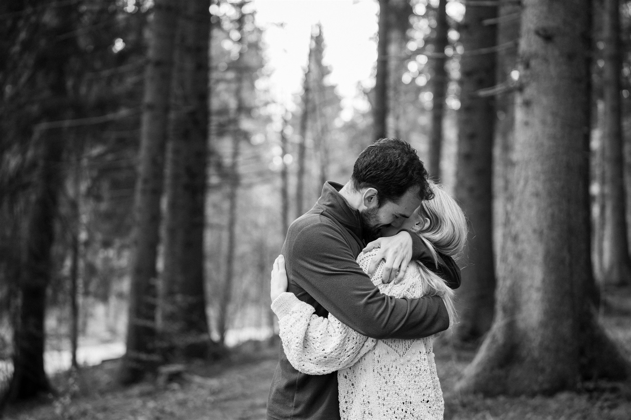 Black-and-white photo of a couple sharing an intimate embrace in the forest