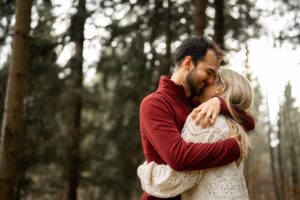 Man embracing his fiancé tightly in the forest while laughing downward