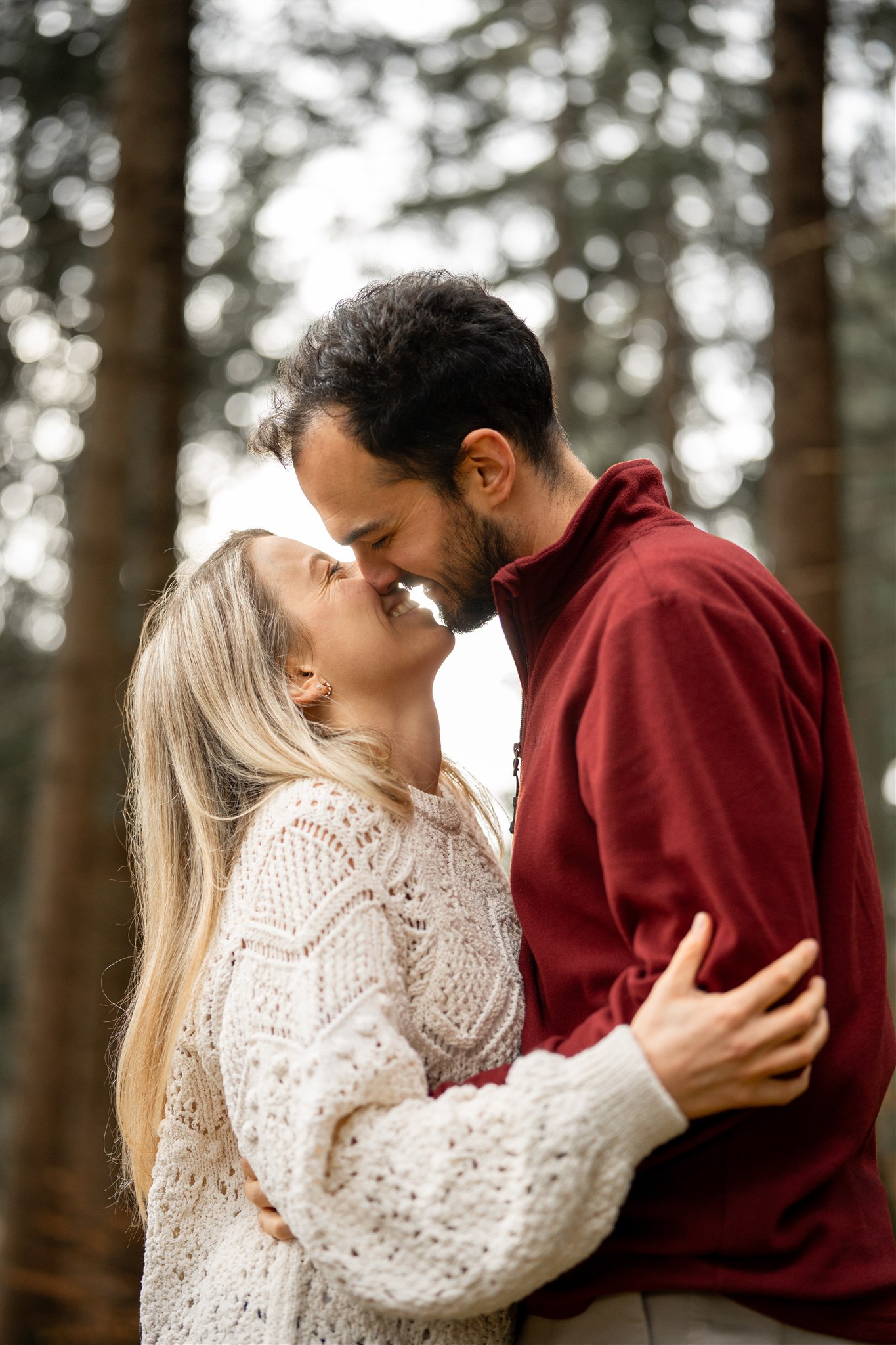Young couple standing arm in arm in the forest while almost kissing