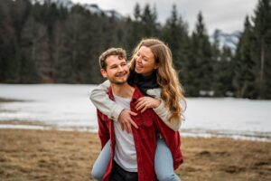Young woman riding piggyback on her fiancé in front of a snowy meadow