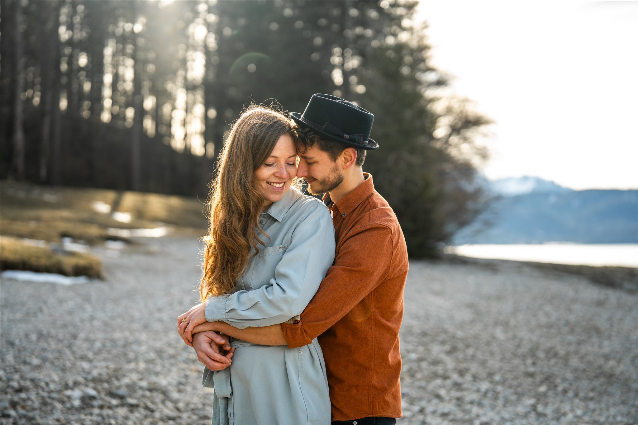 Man embracing his fiancée at sunset by the lakeshore in backlight