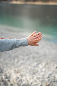 Close-up of hands in front of a turquoise lake with a visible engagement ring