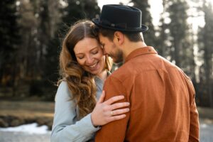 Man whispering into his fiancée’s ear while she smiles and rests her hand on his shoulder