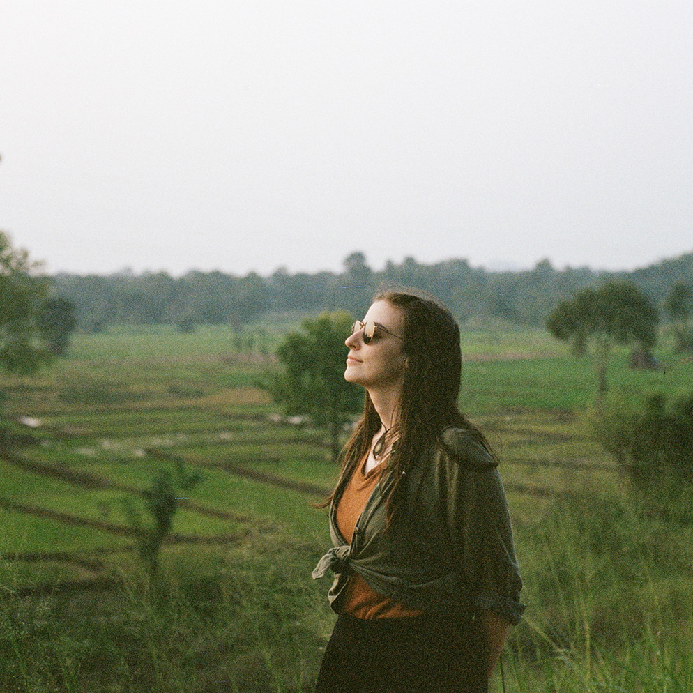 Caro standing in front of rice fields in Asia while gazing dreamily toward the sun
