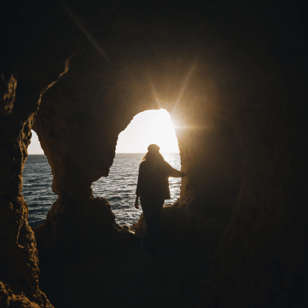 Silhouette of a young woman standing in a cave with sunlight shining through a rock opening