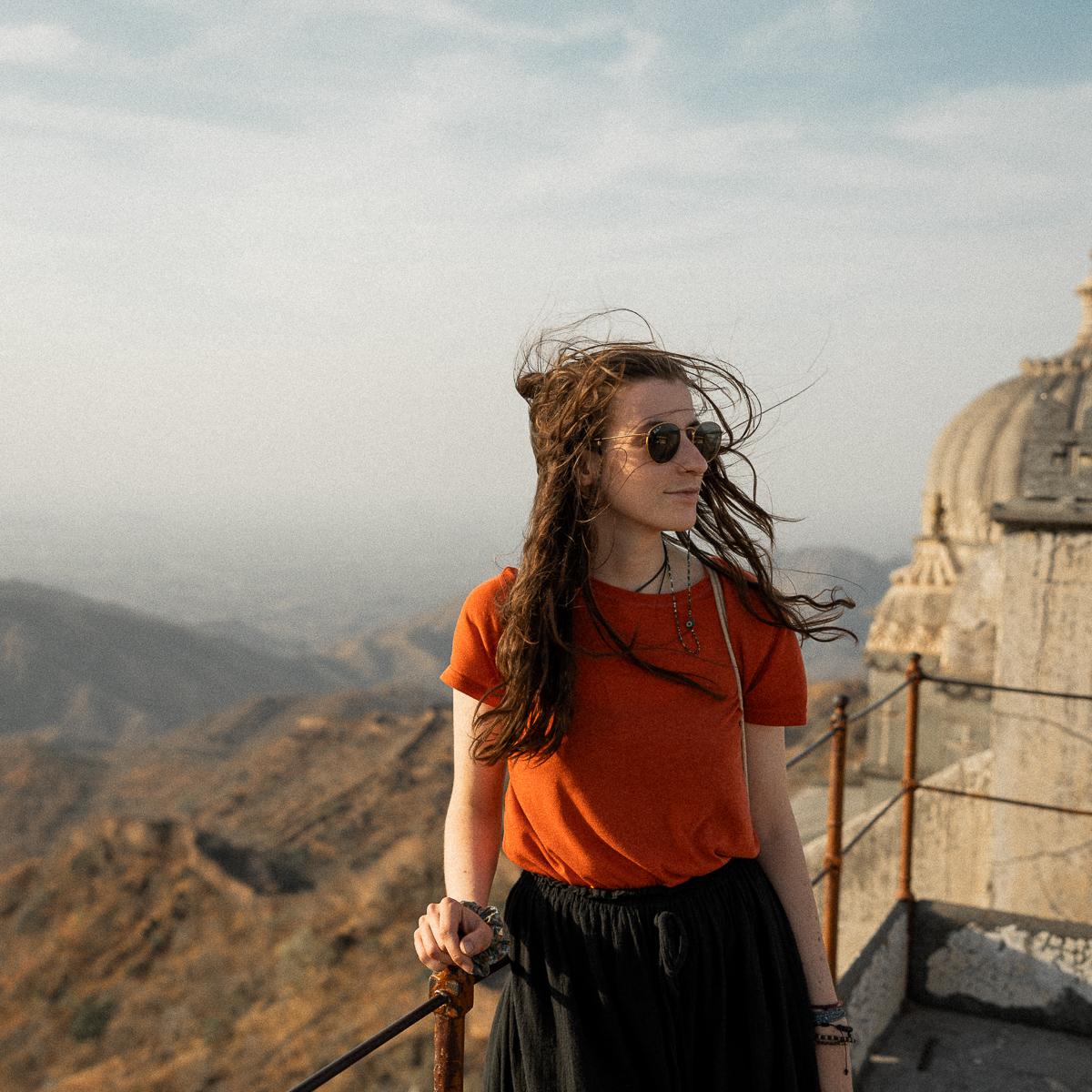 Caro standing on a palace rooftop in India at sunset while the wind blows through her hair