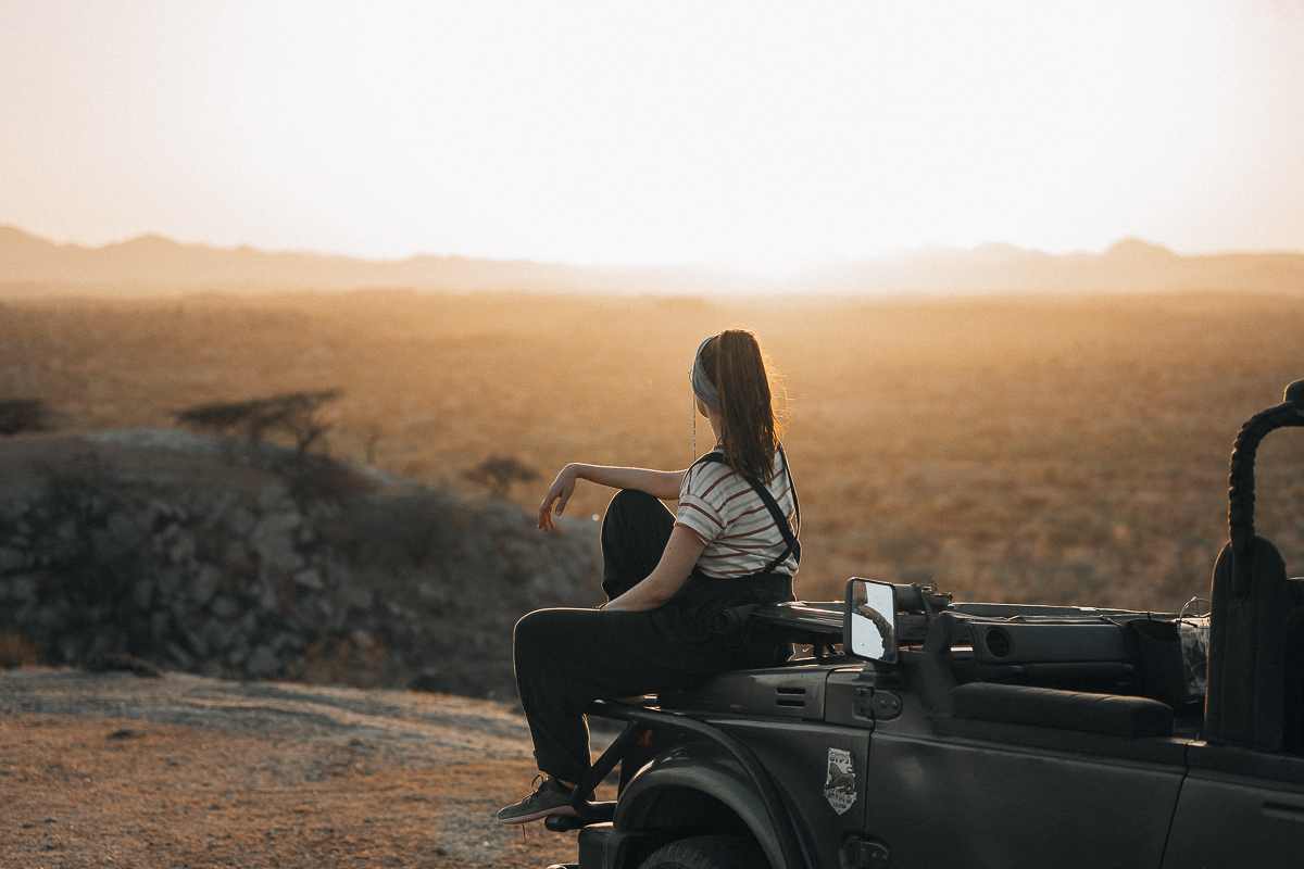 Caro sitting on the hood of a truck at sunset while looking into the golden landscape