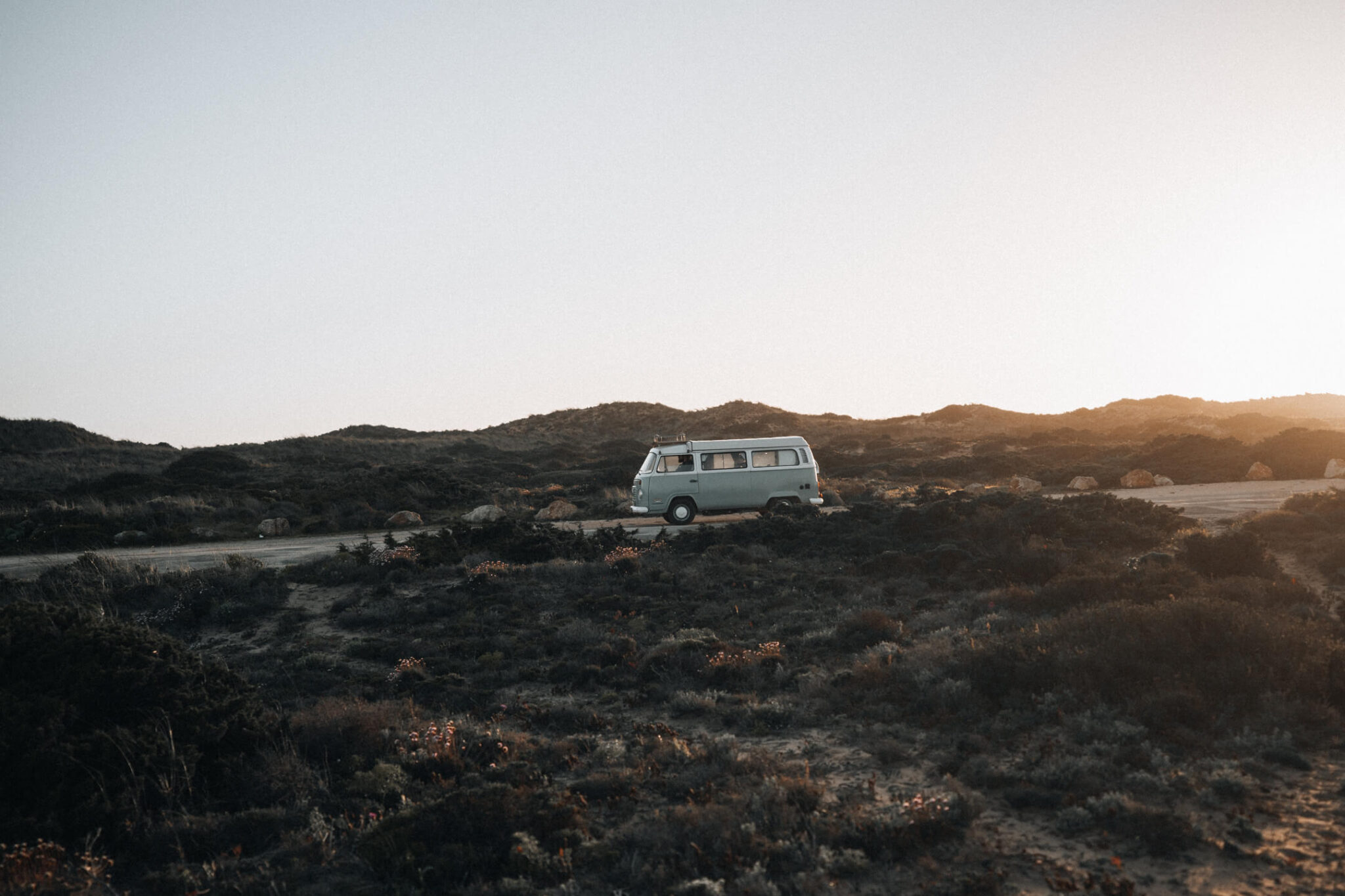 Old VW T2 bus driving down a street in Portugal at sunset