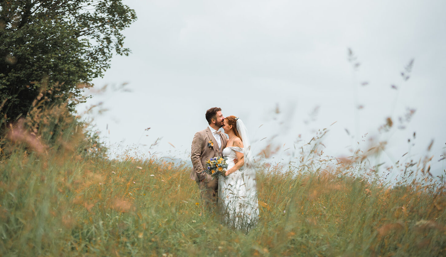 Groom kissing the bride on the forehead in a meadow with green grass and orange flowers