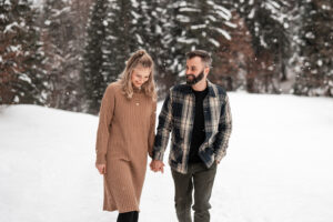 Couple walking through a snow-covered field while the man smiles at his wife