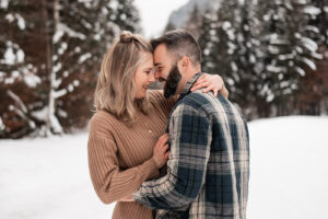 Couple embracing in the snow with their heads leaning together while laughing warmly at each other