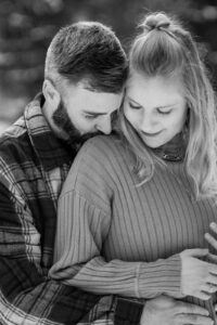 Black-and-white photo of a man embracing his fiancée from behind while both look over their shoulders
