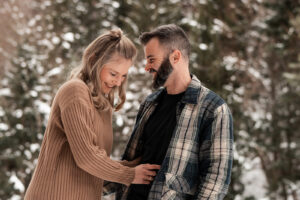 A couple laughing in a snowy landscape while she holds onto him