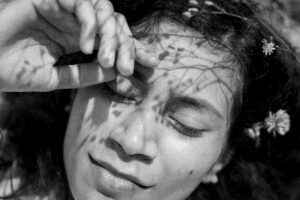 Close-up of a young woman’s face in harsh light with flower shadows cast across her skin