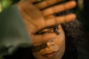 Cinematic photo of a young woman looking upward through her fingers while warm light shines through the trees